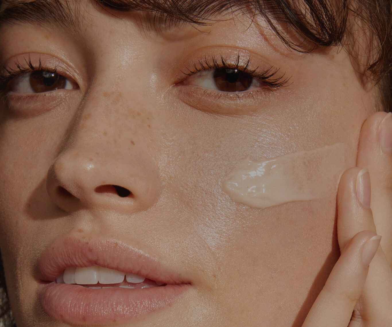 Close up of model smiling applying moisturiser to cleansed skin